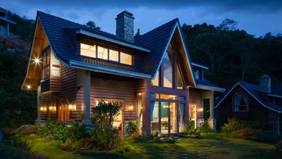 Twilight view of a wood-and-stone two-story house with warm interior lights, lawn, and trees, with no people, logos, or readable text.