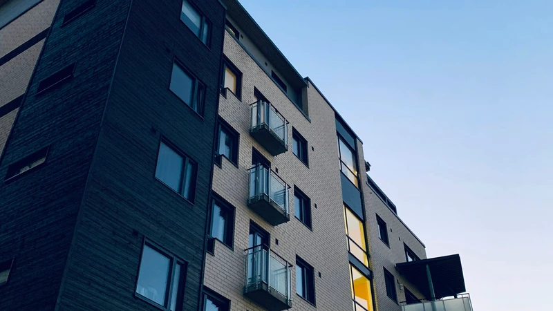 Low-angle exterior of a modern multi-story condominium with glass balconies against a pale sky, with no people, logos, or readable text.