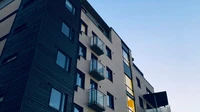 Low-angle exterior of a modern multi-story condominium with glass balconies against a pale sky, with no people, logos, or readable text.