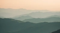 Layered mountain ridges fading into haze at dusk, with no people, buildings, logos, or readable text.