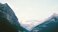 Forested mountain valley with a distant snow-dusted peak and no people, boats, logos, or readable text.