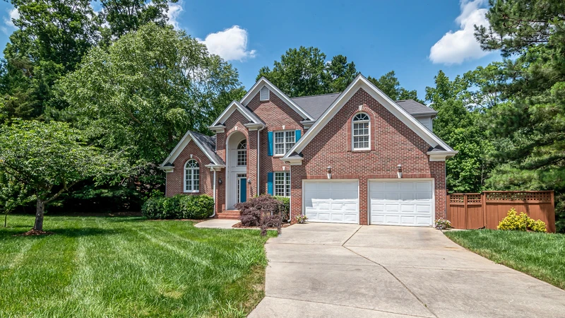 Two-story brick home with a double garage and green lawn on a sunny Tennessee street, no people or text