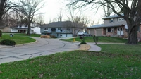 Quiet residential street with two-story houses, bare trees and a curving driveway on a cloudy day, no people or text