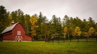 Red wooden barn beside a mowed green field, black fence and autumn trees, no people or text