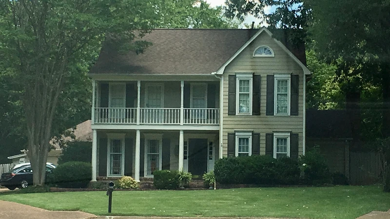 Two-story suburban house with a green lawn and vehicles parked in the driveway