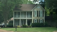 Two-story suburban house with a green lawn and vehicles parked in the driveway