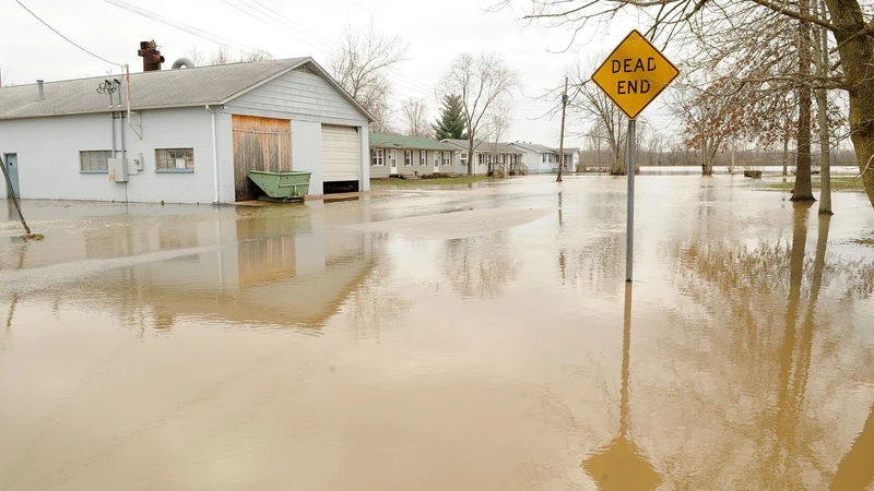 Floodwater covering a neighborhood street past a yellow dead end sign, with a white outbuilding at left
