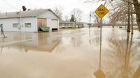 Floodwater covering a neighborhood street past a yellow dead end sign, with a white outbuilding at left