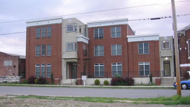 Four-story red brick condominium building with white trim beside a quiet street