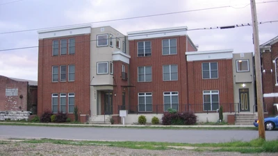 Four-story red brick condominium building with white trim beside a quiet street