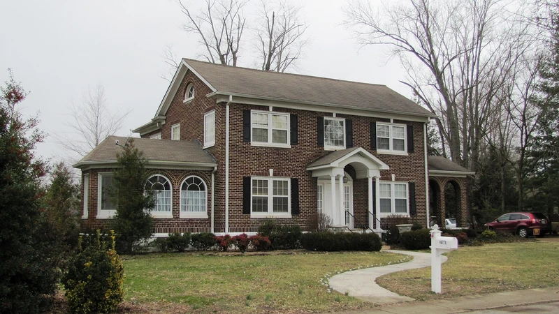 Two-story red brick house with white trim and a front lawn under a cloudy sky