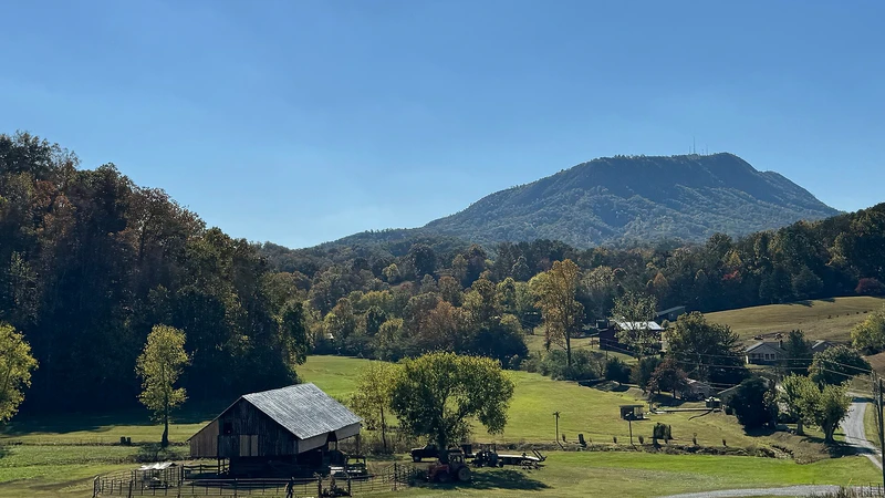 Rural valley with green pastures, a small barn, and forested mountains under a clear blue sky