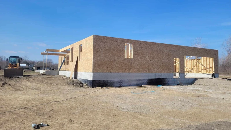 Concrete block building under construction on a cleared dirt lot with equipment nearby