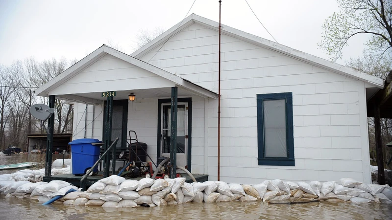White one-story house with a row of sandbags along the front as floodwater surrounds the yard