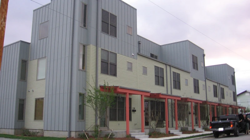 Three-story modern townhome building with metal and stucco siding and red porch railings