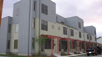 Three-story modern townhome building with metal and stucco siding and red porch railings