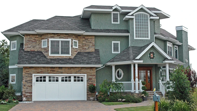 Two-story house with stone and gray siding, a white garage door, and a paved driveway
