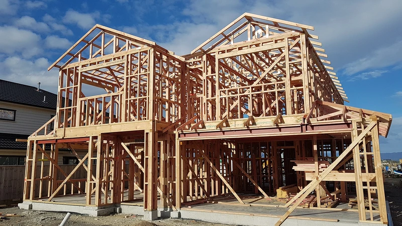 Wood-framed two-story house under construction against a blue sky