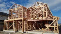 Wood-framed two-story house under construction against a blue sky