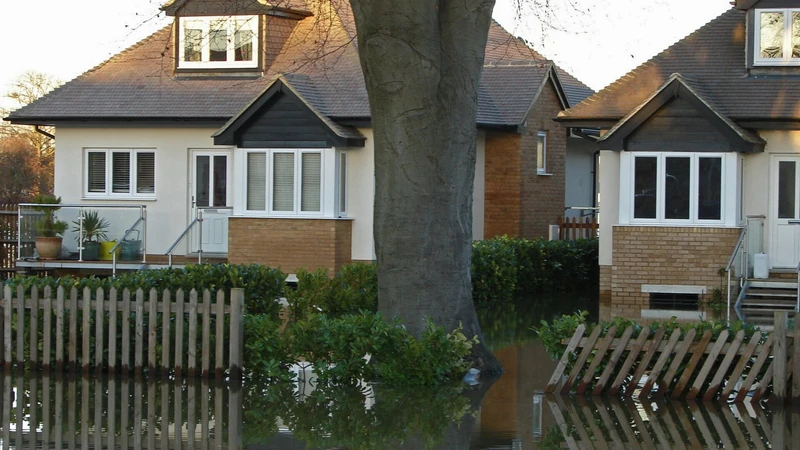 Floodwater standing in front of a row of brick and white-trimmed houses behind a wooden fence
