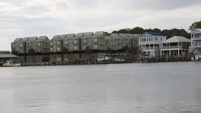Row of multi-story waterfront condominium buildings across a wide river under a gray sky