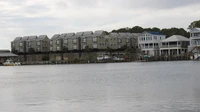Row of multi-story waterfront condominium buildings across a wide river under a gray sky