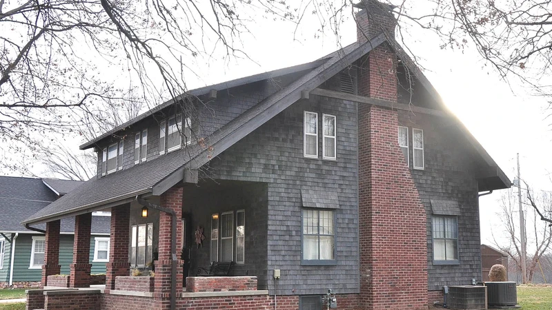 Two-story house with dark shingle siding, a brick chimney, and a covered front porch