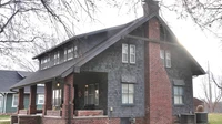 Two-story house with dark shingle siding, a brick chimney, and a covered front porch